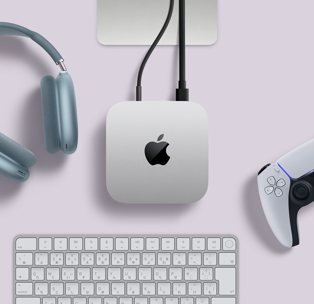 シルバーのMac miniを上から見た図。2本のコードが背面のポートにつながれている。近くにはブルーのAirPods Max、シルバーのMagic Keyboard、ワイヤレスゲームコントローラがある