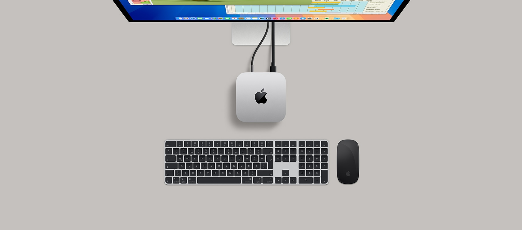 Bir ekrana ba?l? gümü? rengi Mac mini’nin üstten g?rünümü, ekranda oyun oynand??? g?rülüyor ve yan?nda bir kablosuz klavye, bir oyun kumandas? ve mavi bir AirPods Max bulunuyor