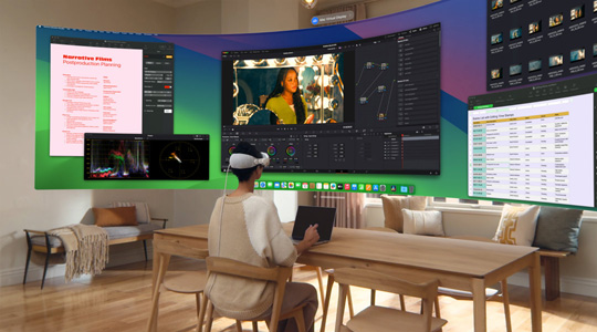 一個人戴著 Apple Vision Pro 坐在桌前，面前是打開的 13 吋 MacBook Pro，螢?zāi)粌?nèi)容以超廣角曲面顯示器方式投影在房間內(nèi)