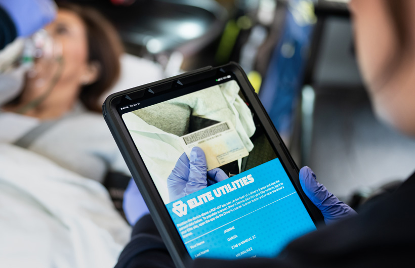La app Elite Utilities está abierta en el iPad y una persona de emergencias escanea el carné de conducir de una paciente tumbada en una camilla